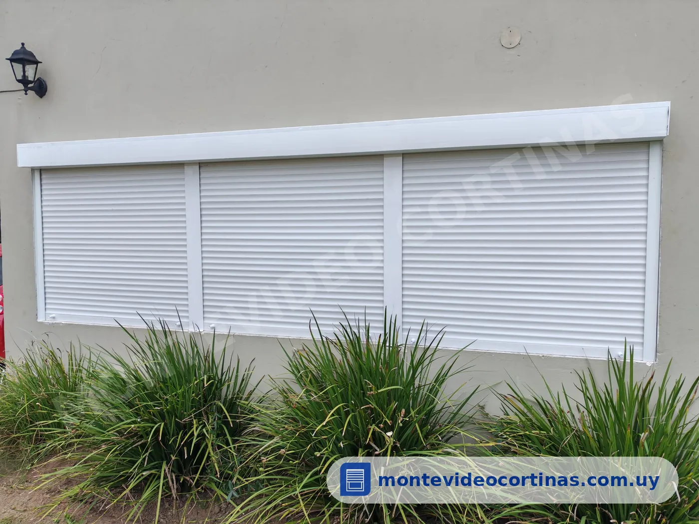 Tres cortinas de enrollar blancas instaladas en una fachada con jardín